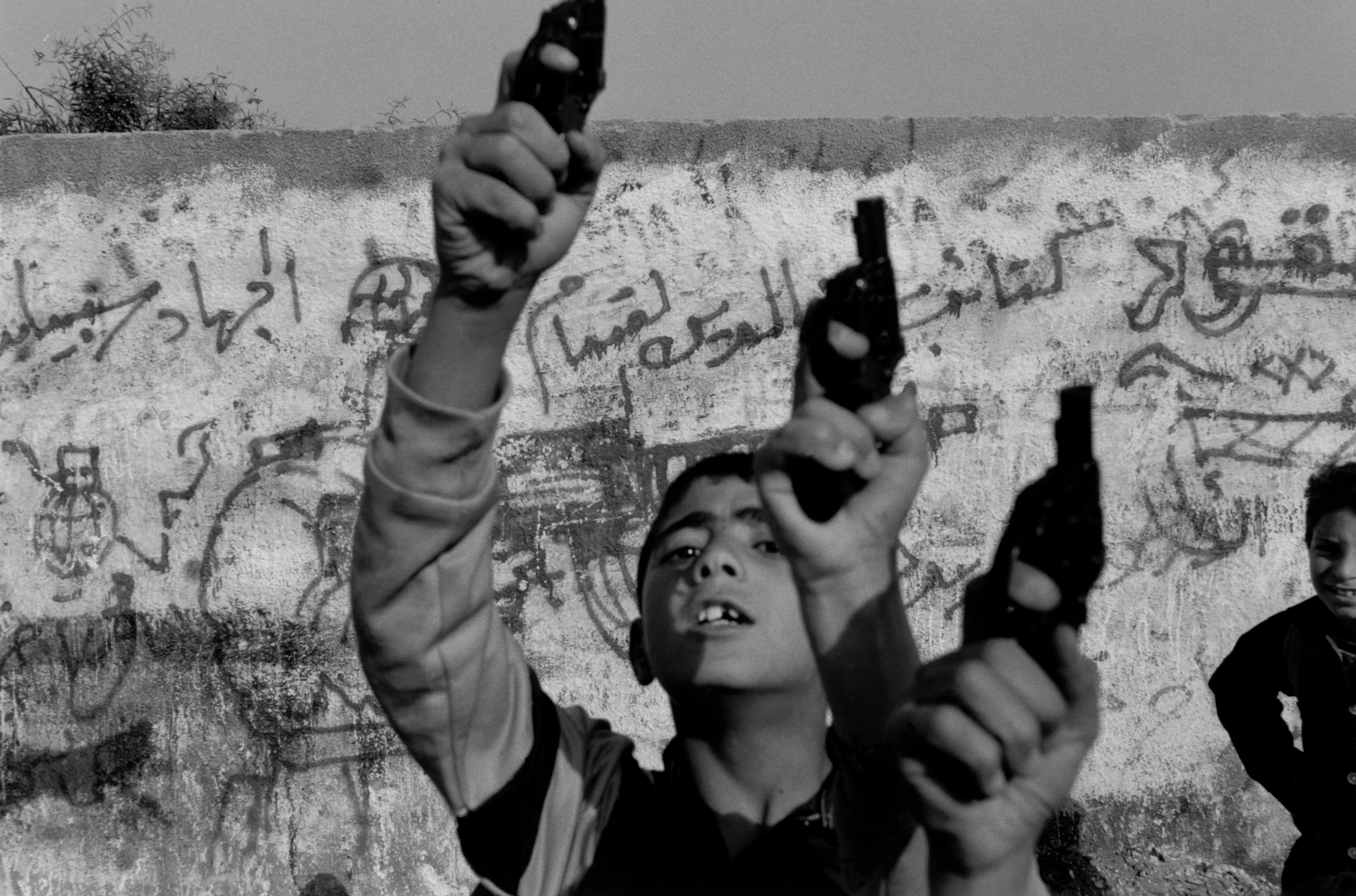 Fine Print: Children holding toy guns in the air. Palestine, 1993