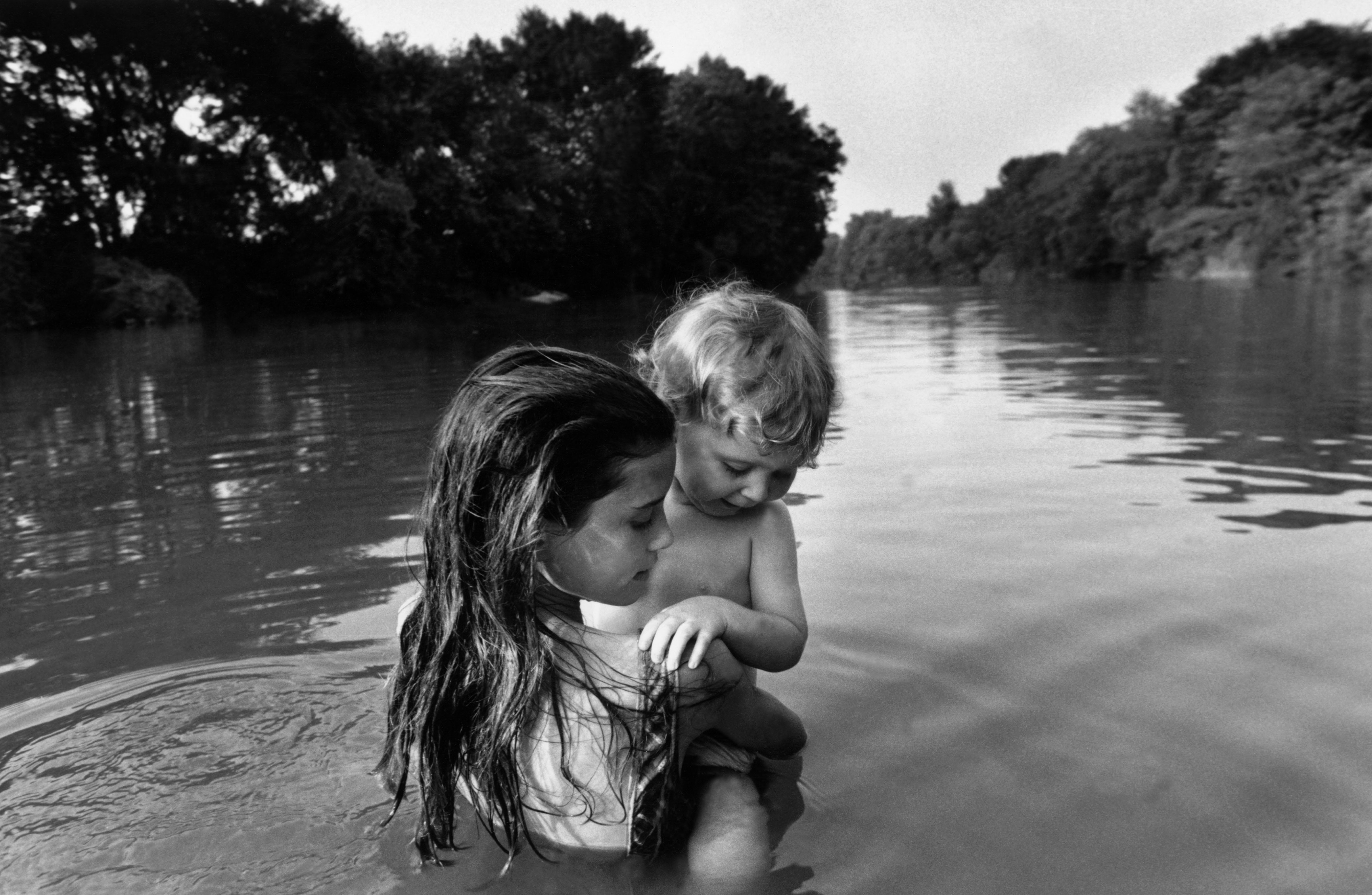 Fine Print: Two-year-old Isaac Towell is carried into the Sydenham River by his older sister Naomi to introduce him to water. Lambton County, Ontario, Canada, 1996